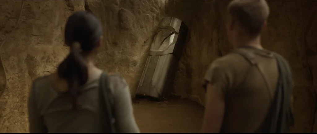Two explorers standing in a cave, looking at a metallic sarcophagus embedded in the rock wall, scene from the film Sanctuary